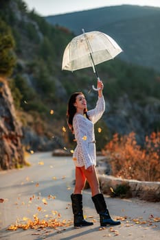 woman umbrella leaves , She holds him over her head, autumn leaves are falling out of him. Beautiful woman in a dress with an umbrella in the autumn park on the road in the mountains