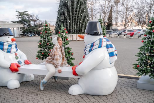 Woman Christmas Square. Close-up of a winter white toy snowman With trees decorated with Christmas tinsel in the background.