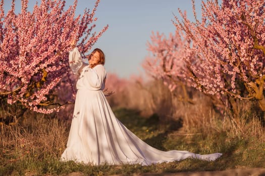 Woman blooming peach orchard. Against the backdrop of a picturesque peach orchard, a woman in a long white dress enjoys a peaceful walk in the park, surrounded by the beauty of nature