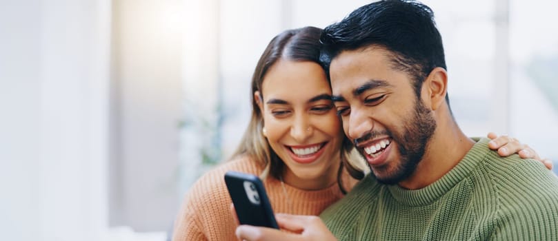 Love, hug and happy couple with phone in a house for social media, streaming or checking meme in their home together. Smartphone, app and people smile in a living room for funny gif, text or chat.