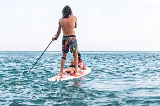 Sea woman and man on sup. Silhouette of happy young woman and man, surfing on SUP board, confident paddling through water surface. Idyllic sunset. Active lifestyle at sea or river