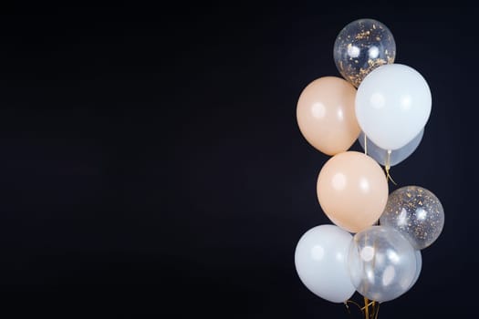 A bunch of balloons in white, beige and transparent colors on a dark background with space for an inscription. High quality photo