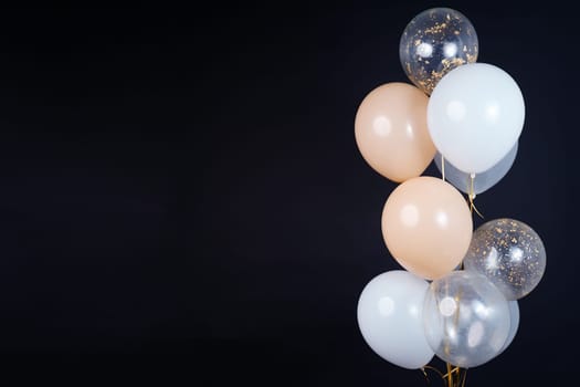 A bunch of balloons in white, beige and transparent colors on a dark background with space for an inscription. High quality photo