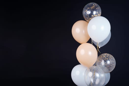 On a black background, balloons of light shades - white, beige, transparent - are flying. Space for text. High quality photo