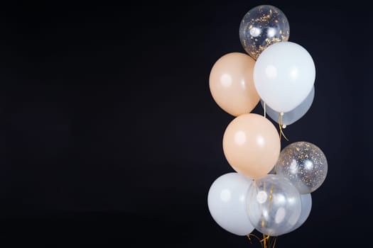 On a black background, balloons of light shades - white, beige, transparent - are flying. Space for text. High quality photo