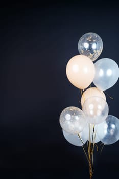 On a black background, balloons of light shades - white, beige, transparent - are flying. Space for text. High quality photo