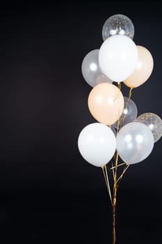 A bunch of balloons in white, beige and transparent colors on a dark background with space for an inscription. High quality photo