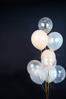 On a black background, balloons of light shades - white, beige, transparent - are flying. Space for text. High quality photo