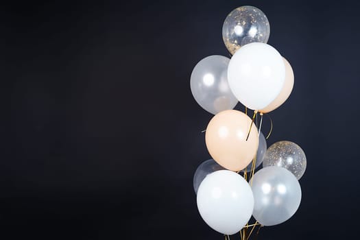 On a black background, balloons of light shades - white, beige, transparent - are flying. Space for text. High quality photo