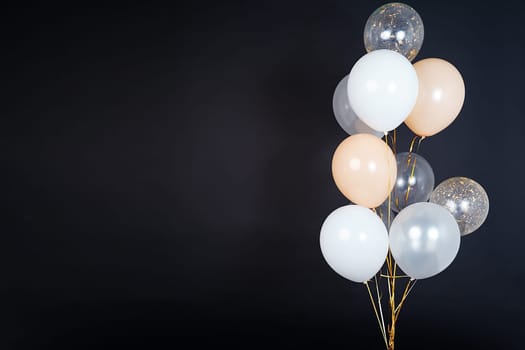 A bunch of balloons in white, beige and transparent colors on a dark background with space for an inscription. High quality photo