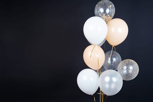 A bunch of balloons in white, beige and transparent colors on a dark background with space for an inscription. High quality photo