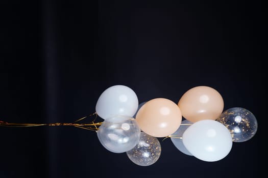 A bunch of balloons in white, beige and transparent colors on a dark background with space for an inscription. High quality photo