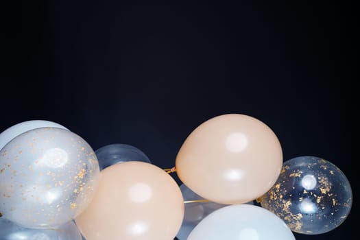 On a black background, balloons of light shades - white, beige, transparent - are flying. Space for text. High quality photo