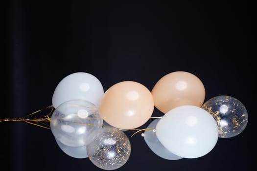 A bunch of balloons in white, beige and transparent colors on a dark background with space for an inscription. High quality photo