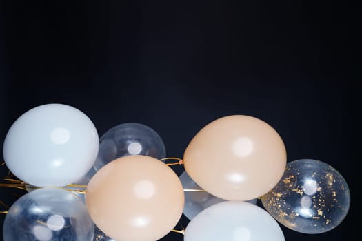 On a black background, balloons of light shades - white, beige, transparent - are flying. Space for text. High quality photo