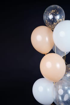 On a black background, balloons of light shades - white, beige, transparent - are flying. Space for text. High quality photo