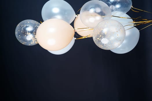 On a black background, balloons of light shades - white, beige, transparent - are flying. Space for text. High quality photo