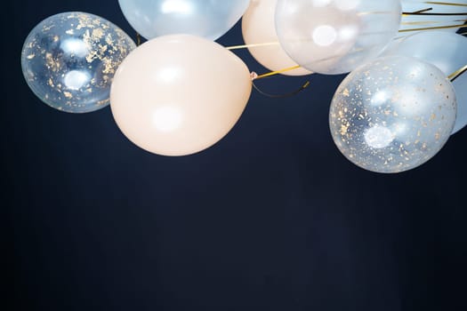 On a black background, balloons of light shades - white, beige, transparent - are flying. Space for text. High quality photo