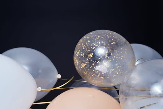 On a black background, balloons of light shades - white, beige, transparent - are flying. Space for text. High quality photo