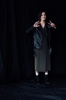 woman in dark clothes posing on a black background shows two