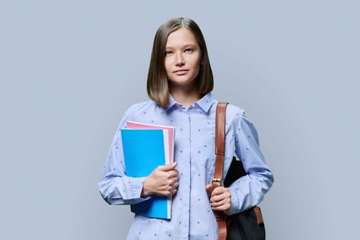 Portrait of young university student with backpack of textbooks on gray studio background. Smiling confident positive 20s female looking at camera. Education, knowledge, lifestyle, youth concept