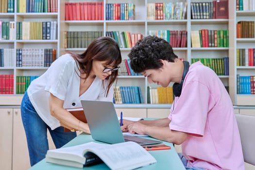 Woman teacher mentor talking teaching helping male student in college library, lesson, exam preparation. Knowledge, education, youth, college university concept