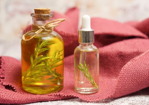 bottle and dropper with rosemary oil with fresh twigs inside on a red cloth