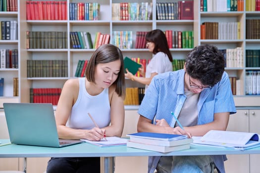 College students guy and girl study in library. Students prepare for an exam, write, read, and type on laptop. Education, knowledge, learning, youth concept