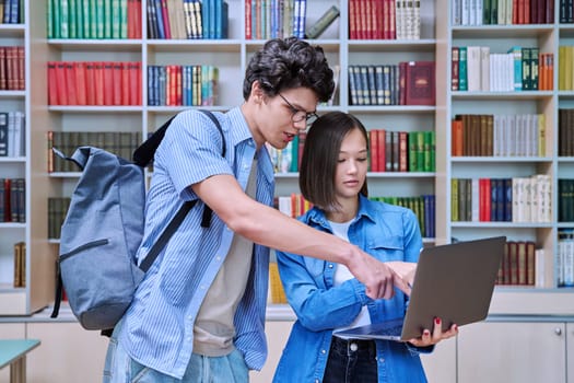 Young students male and female in college library talking, studying, preparing for exams, with laptop. Knowledge, education, youth, college university concept