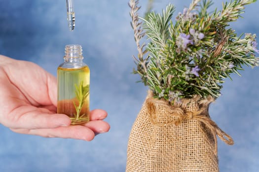 woman holds a dropper with rosemary essential oil with fresh branches inside a drop falls from the pipette