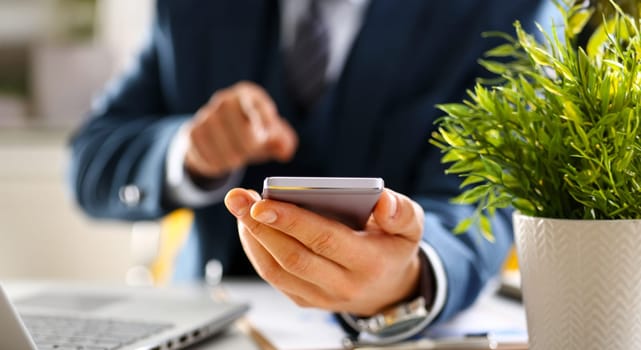 Male arm in suit hold phone and silver pen at workplace closeup. Read news mania send sms chat addict use electronic bank modern lifestyle job plan colleague share blog tweet web application search