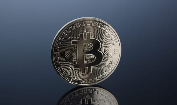 Coin of crypto currency bitcoin on a gray-blue background with reflection subject gold exchange pyramid on money in connection with the growth or fall exchange rate closeup.