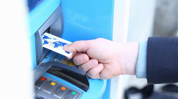 Male hand hold white credit card aganist ATM background.