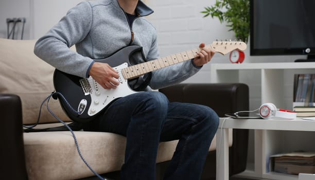 Male hands at home play and tune the electric guitar is engaged in music realizes listening enjoying music notation large concept closeup