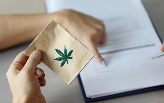 Focus on male hand giving package with cannabis sign on it. Doctor writing treatments appointment and showing sign place for patient. Healthcare and medical marijuana concept