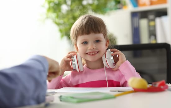 Satisfied child in headphones sitting at home table and looking into camera portrait.