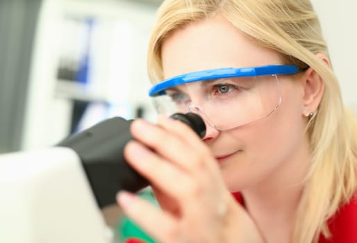 Female chemist in glasses look at microscope aganist chemistry background. Pharmaceutical research concept