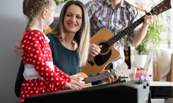 Portrait of happy smiling mother looking at little daughter with happiness and gladness. Parents with child playing on musical instruments and having fun. Parenthood and childhood concept