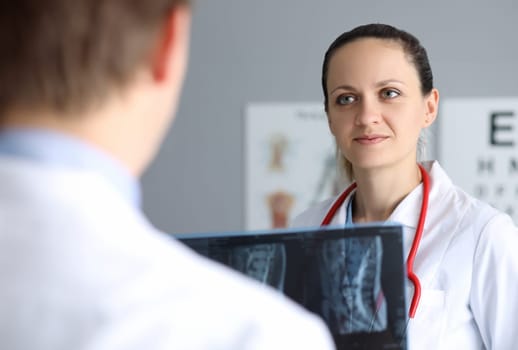 Portrait of cute female physician smiling and looking at colleague with gladness. Male doc holding in hands x-ray of patient. Medicine and healthcare concept