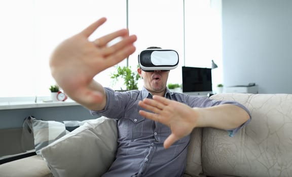 Man sits at home on the couch uses virtual reality glasses rides on a roller coaster screaming in fear. Software tester concept