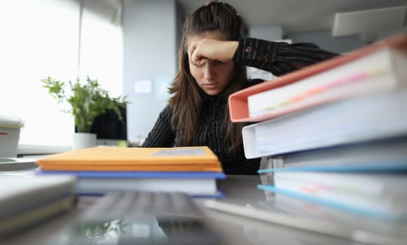 Close-up of young tired businesswoman sitting at workplace with bunch of important documents. Female with tight schedule. Job office style and business concept