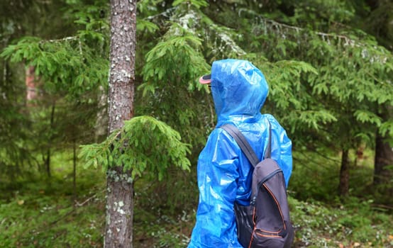 Woman in blue protective polyethylene raincoat agains forest background. Search for get missing people concept