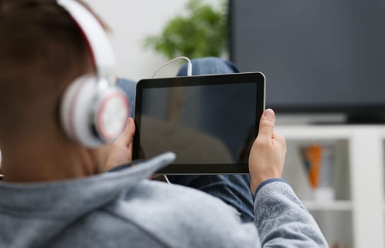 Male hand holds tablet pad in home setting while sitting on the couch engaged an internet surfing using application to press a finger on the display leisure listering music concept closeup.