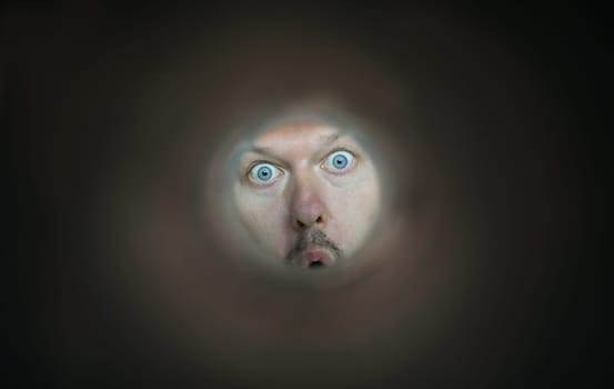 Focus on facial expression of person. Young guy with blue eyes looking through thin tube. Cheerful character with mustache and open mouth. Humorous person