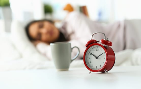 Beautiful indian woman peacefully lying in bed sleeping early morning while alarm clock going to ring awakening. Early wake up, not getting enough sleep, oversleep, getting work time concept