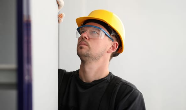 Portrait of man dealing with apartment remodeling and betterment. Person wearing helmet and protective glasses seriously looking at corner. Workman with gloves