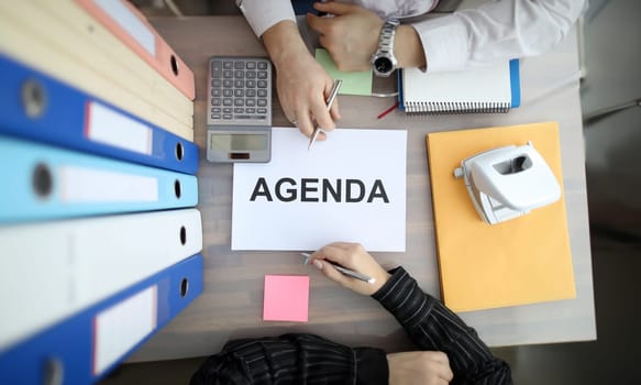 Two business people hand on office table with sign AGENDA paper top view background. Business planning concept