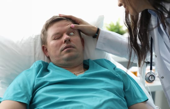 Close-up of ill patient lying in hospital ward. Professional doctor making eyeballs examination. Serious woman in medical gown. Healthcare and treatments concept