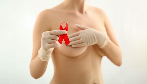 Female hand in gloves holding red ribbon cancer symbol breast closeup on doctor mammology clinic reception. Mammary glands test biopsy implant silicone insert tumor human concept