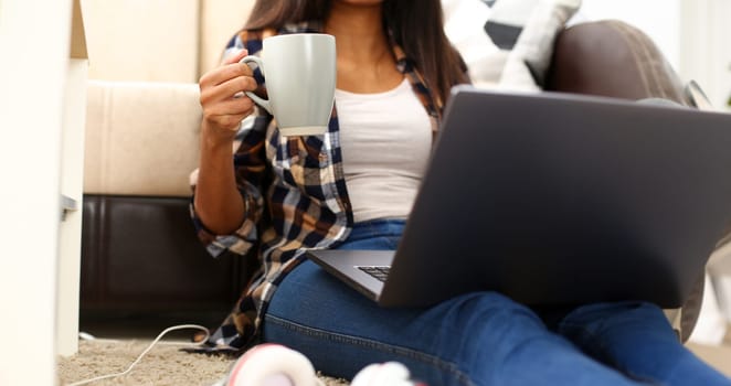 Black woman hold in hand cup of fresh aroma coffee sitting on floor at home having good time lifestyle concept